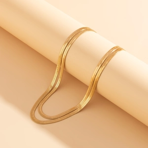 Detail of double-layer golden snake chain necklace on beige cylindrical display stand