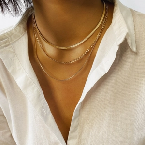 Close-up of layered gold herringbone and figaro chain necklaces on a white shirt