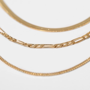 Close-up of gold snake bone, figaro and round link necklaces in a minimalist trio set