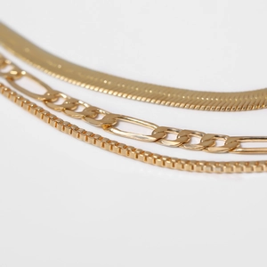 Detail of layered gold necklaces featuring herringbone, figaro, and box chain textures