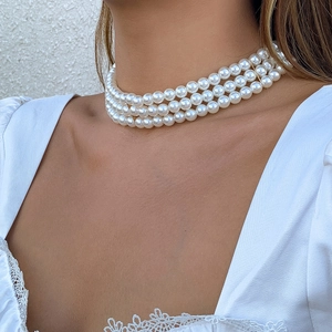 Detalle de gargantilla multicapa de perlas blancas estilo boho sobre encaje blanco