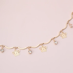 Dettaglio di una collana dorata con ciondoli a farfalla traforati e strass bianchi lucidi