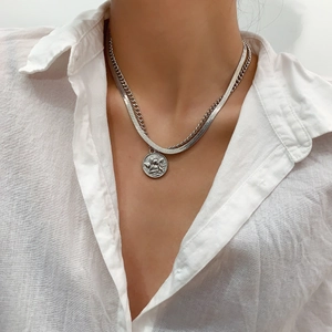 Detail of layered silver snake chain with embossed angel coin pendant on a model
