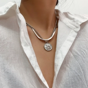Close-up of layered silver snake chain necklace with embossed angel coin pendant
