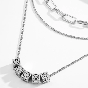 Collar de capas de acero inoxidable con colgantes de dados sonrientes en fondo blanco