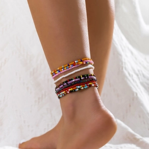 Detailansicht bunter handgefertigter Boho-Perlen-Fußkettchen am Knöchel auf weißem Stoff