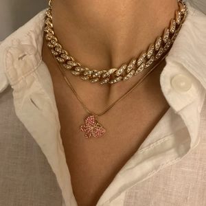 Detail einer geschichteten Goldkette mit rosa Schmetterlingsanhänger und glänzender Panzerkette