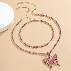Detail einer doppelten Goldkette mit funkelndem rosa Schmetterlingsanhänger
