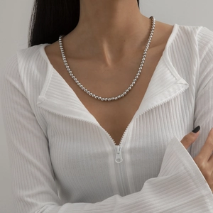 Nahaufnahme einer glänzenden silbernen Perlenkette an einem Model in weißer Kleidung