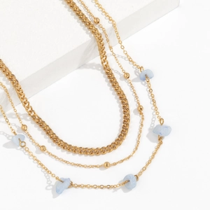 Detail of layered gold cuban chain with light blue natural stones on a white stand