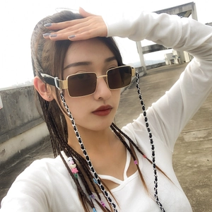 Détail de lunettes de soleil dorées avec chaîne tressée noir et blanc de style punk
