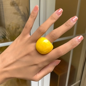 Nahaufnahme eines breiten neongelben Acrylrings am Finger eines Models bei warmem Licht