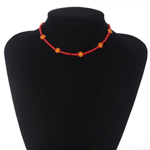 Detail van boheemse rode kralenketting met oranje madeliefjes op een zwarte halsdisplay