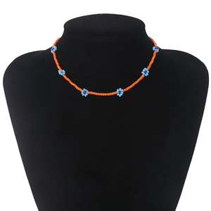 Detail van boheemse oranje kralenketting met blauwe madeliefjes op een zwarte mannequin