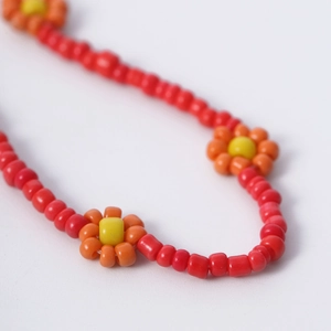 Detailopname van rode kralenketting met oranje madeliefjes in bohemien stijl