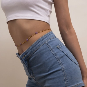 Detail of bohemian gold waist chain with purple daisy charms on model with blue jeans
