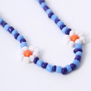 Detail van de blauwe kralenketting met handgemaakte madeliefjes en gouden slotje