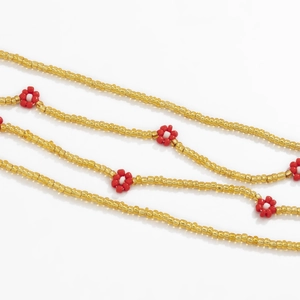 Macro shot of Bohemian waist chain featuring delicate red beaded flowers and gold accents