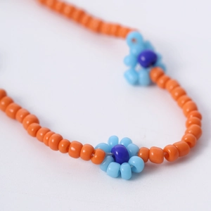 Detailopname van de bohemien kleurrijke madeliefjesketting met oranje en blauwe kralen