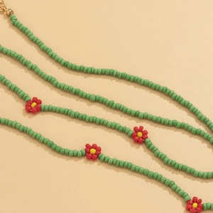 Detail of colorful beaded waist chain featuring red and yellow daisy charms on green beads