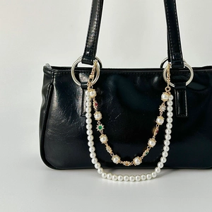 Close-up of double-layer faux pearl and floral gold metal chain strap on black bag