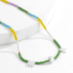 Detail van kleurrijke boho kralenketting met witte hartvormige hanger en letters M en A