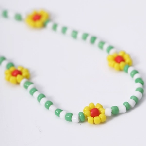 Detailopname van boheemse kralenketting met groen-witte buisjes en gekleurde madeliefjes