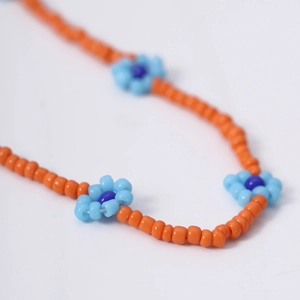Detail macro-opname van Boheemse oranje kralenketting met blauwe madeliefjes als hangers