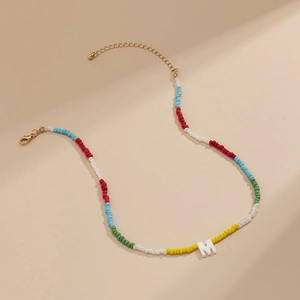 Detail van kleurrijke regenboog kralenketting met een witte letter M hanger en goudkleur