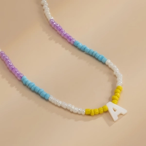 Detailopname van kleurrijke kralenketting met witte letter A hanger op beige achtergrond