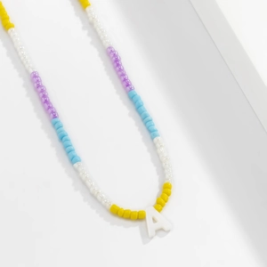 Detail van de kralenketting met kleurrijke kralen en een witte hars letter A hanger
