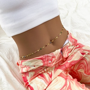Detail of a gold body chain featuring multicolored heart charms worn with stylish pants
