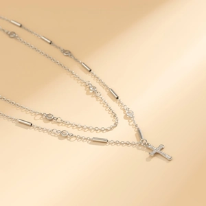 Close-up of a silver double-layer chain with a crystal cross pendant and zircon beads