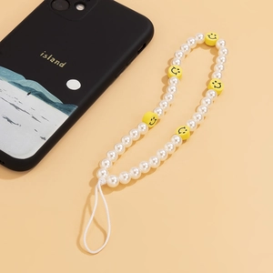 Close-up of white imitation pearl phone charm with yellow smiley face beads on beige surface