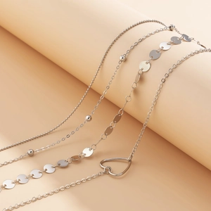 Détail d'un collier multicouche argenté avec pendentif cœur et disques de paillettes