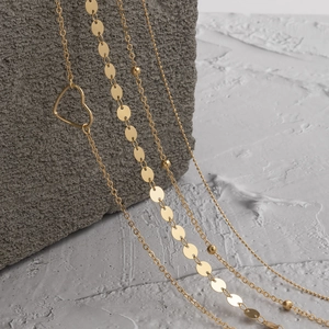 Détail macro de chaînes dorées avec pendentif cœur et paillettes sur pierre