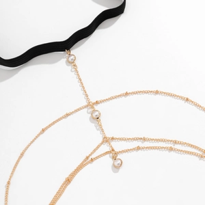 Detail van gouden beenketting met parels en zwarte elastische band voor op het strand