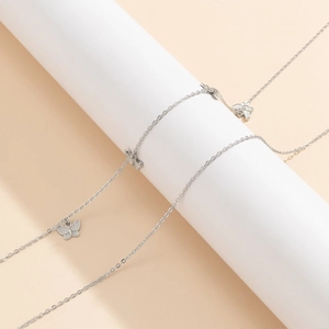 Gros plan des pendentifs papillons argentés et de la chaîne fine sur socle blanc