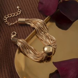 Detail van gelaagde gouden armband met gepolijste bol op een dienblad in vintage stijl