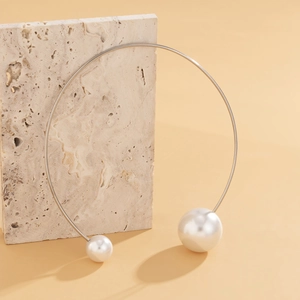 Detail view of a silver choker featuring two asymmetric pearls on a warm stone background