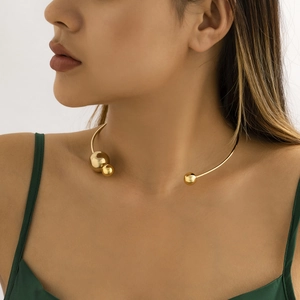 Detail of asymmetric gold choker with smooth metallic beads on a female model