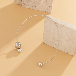 Minimalist silver choker detail featuring asymmetrical spheres on a textured stone surface