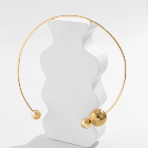 Close-up of golden minimalist choker with asymmetrical metallic pearls on white wavy stand