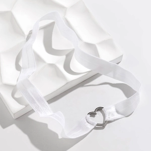 Détail macro d'une sangle élastique blanche avec boucle en cœur argentée sur socle