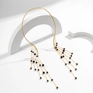 Detail van gouden metalen choker met lange kettingkwastjes en zwarte kralen op wit decor