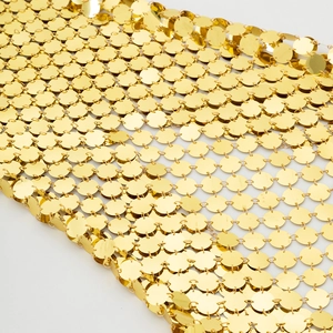 Detailopname van gouden metalen lovertjes geweven in een flexibele bodychainstructuur