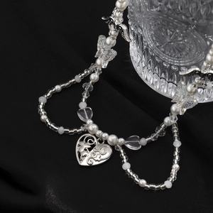 Detalle de colgante de corazón plateado con mariposa y perlas sobre un fondo de tela negra