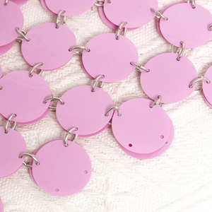 Nahaufnahme von rosa Pailletten mit silbernen Metallringen auf weißem Strickstoff