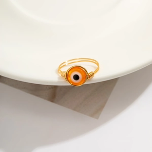 Detail of a handmade gold wire wrapped ring with an orange evil eye bead centerpiece