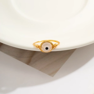 Detail of handcrafted gold wire wrapped ring with evil eye bead on white ceramic